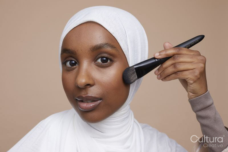 Studio portrait of young woman in white hijab applying make-up