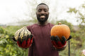 Portrait of smiling man holding pumpkins in urban garden
