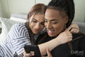 Two young women on bed looking at smart phone