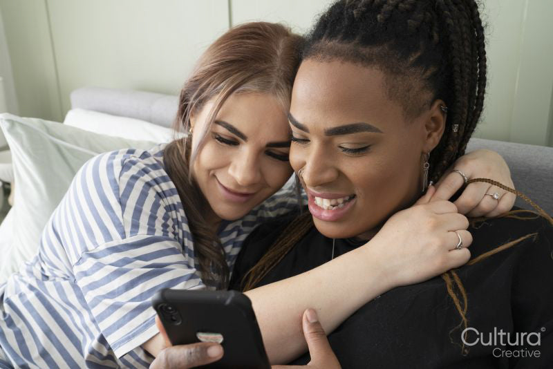 Two young women on bed looking at smart phone