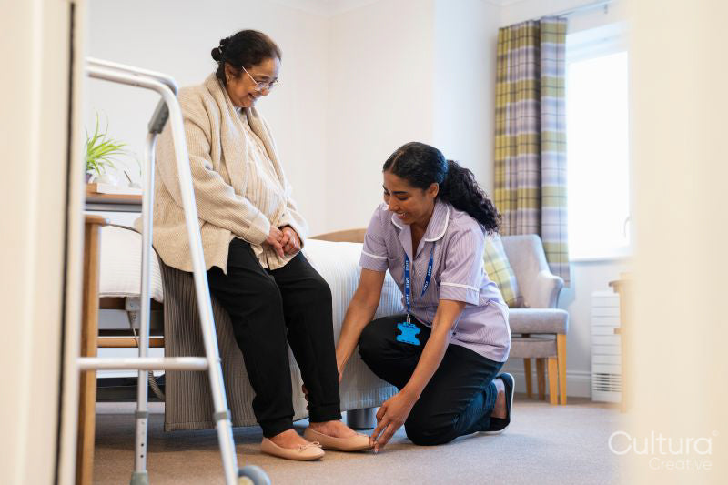 Nurse helping senior lady to put on her shoes at nursing home