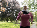 Sutton,Woman in headscarf and headphones jogging in park