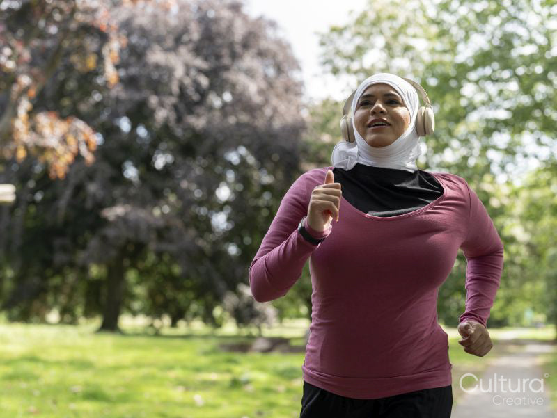Sutton,Woman in headscarf and headphones jogging in park