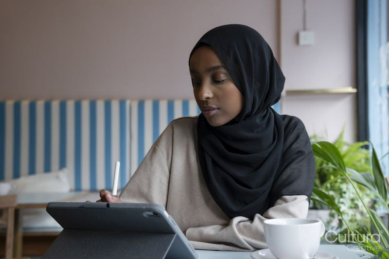 Young woman in hijab working on tablet in cafe