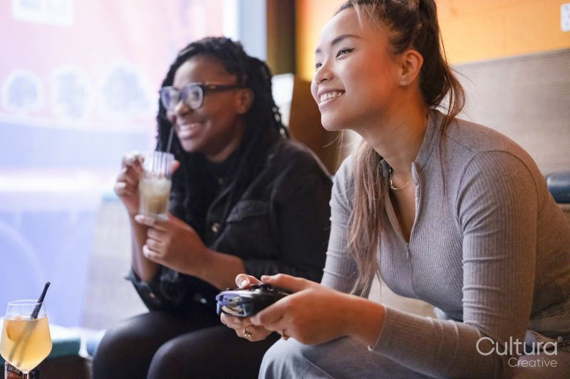 Female friends drinking cocktails and playing in video games at pub