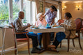Nurse visiting group of seniors dining at cafeteria in nursing home
