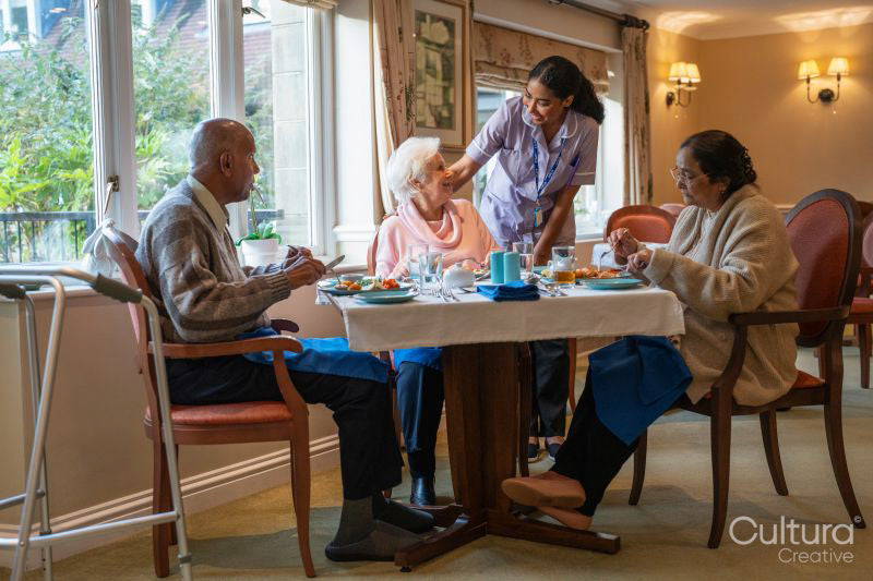 Nurse visiting group of seniors dining at cafeteria in nursing home