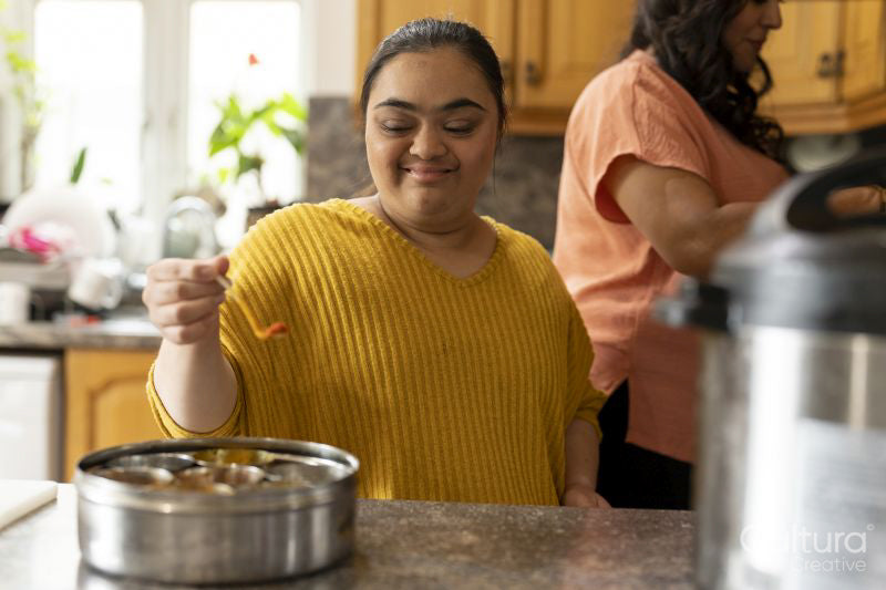 Woman with down syndrome adding spices while cooking with mother in kitchen