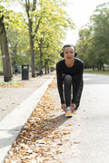 Portrait of woman in sports clothing and headphones tying shoe in park
