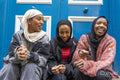 Three smiling women wearing hijabs sitting in front of blue door