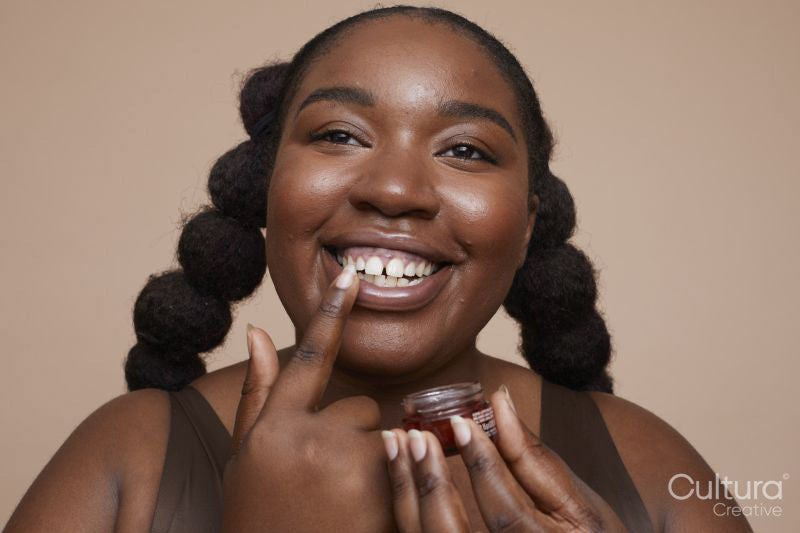 Studio shot of smiling young woman applying lip moisturizer