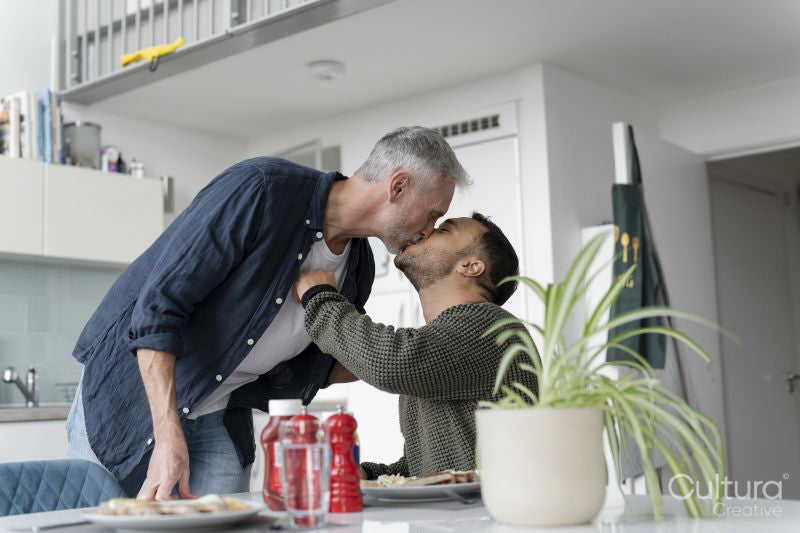 Male couple kissing and eating breakfast at home