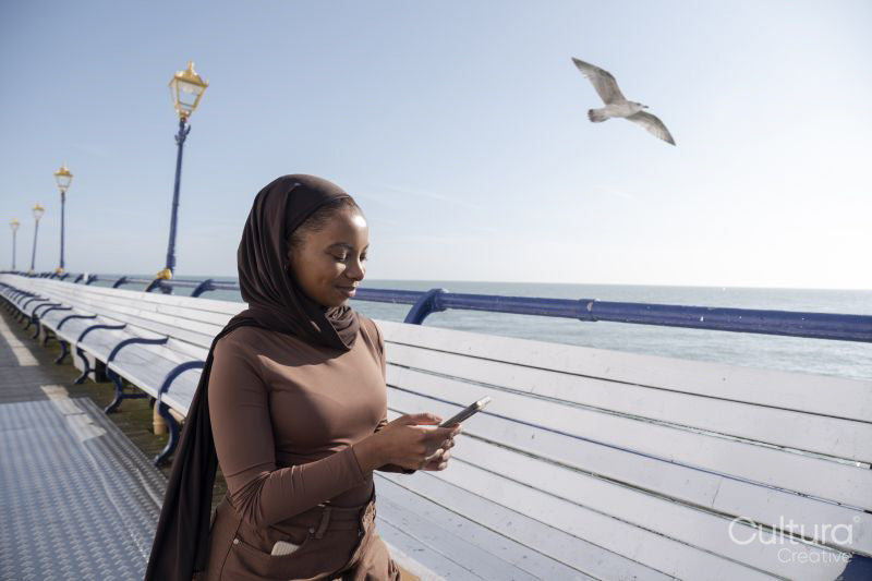 Muslim woman using smart phone while standing on pier on sunny day