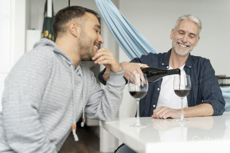 Male couple pouring red wine at home