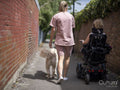 Woman in electric wheelchair going on walk with dog and assistant