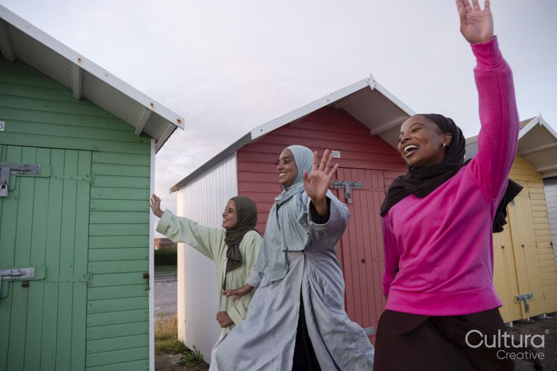 Cheerful Muslim friends waving while walking next to beach huts