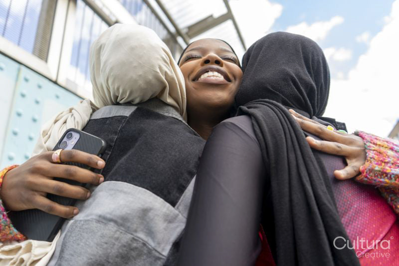 Young women wearing hijabs hugging in city