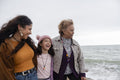 Grandmother, mother and daughter walking on beach on cloudy day