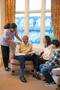 Senior man sitting in armchair surrounded by family and care giver in retirement home