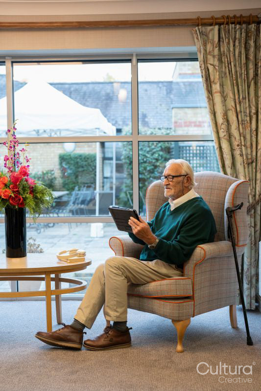 Senior man sitting in armchair and using tablet in nursing home