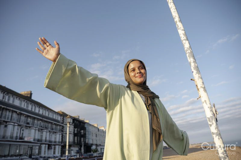Portrait of smiling Muslim woman standing with arms outstretched on sunny day