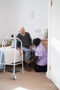 Caregiver helping senior man sitting on bed to put on shoes