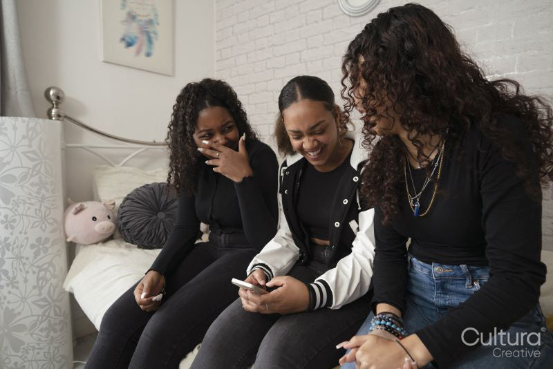 Laughing teenage girls using smart phone in bedroom