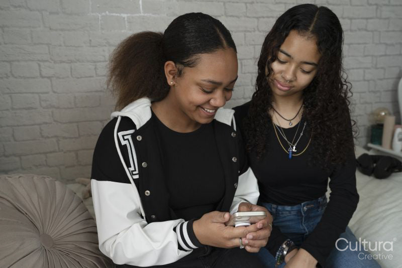 Two friends using smart phone on bed at home