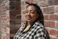 Portrait of smiling woman wearing plaid shirt leaning against brick wall