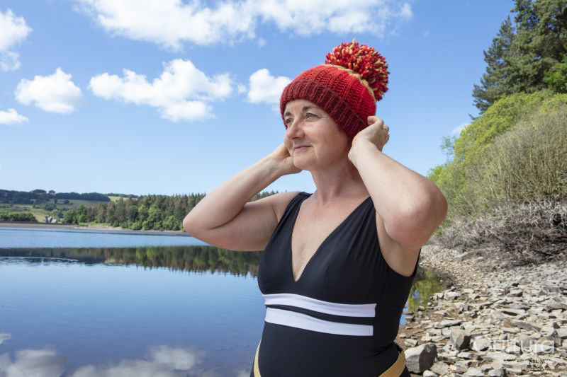 Woman in swimsuit and knit hat on lakeshore, Yorkshire, UK