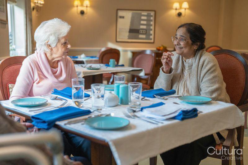 Two senior ladies talking and dining at cafeteria in nursing home