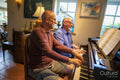 Senior male couple playing piano at home
