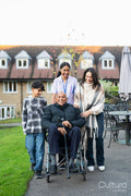 Senior man sitting in wheelchair surrounded by family and care giver outside retirement home