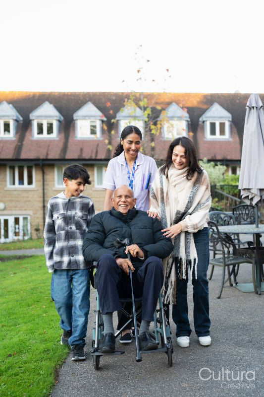 Senior man sitting in wheelchair surrounded by family and care giver outside retirement home