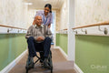 Female care giver pushing senior man in wheelchair in nursing home
