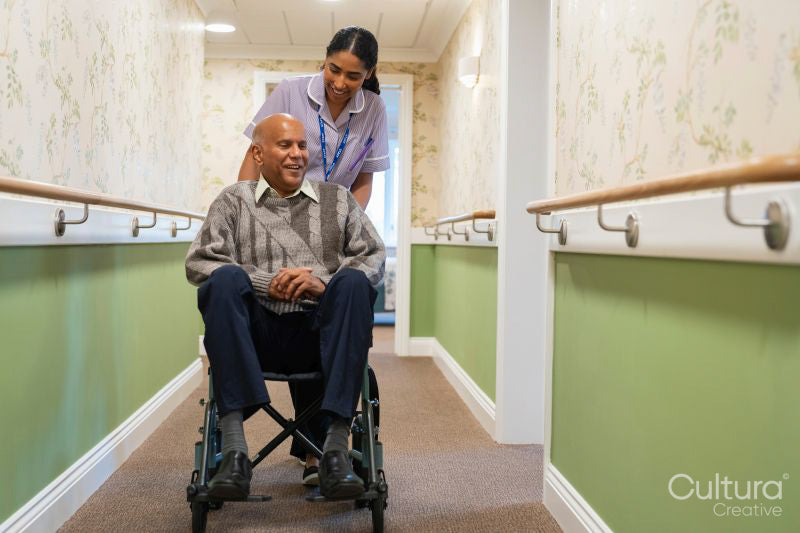 Female care giver pushing senior man in wheelchair in nursing home