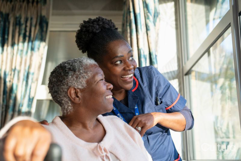 Senior woman and nurse looking through window in nursing home