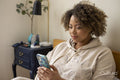 Woman sitting on bed and looking at smart phone