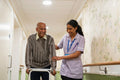 Care giver assisting senior man while walking along corridor in nursing home
