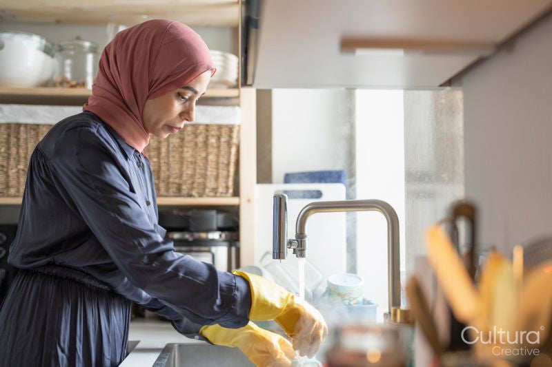 Mid adult woman in hijab washing dishes at home