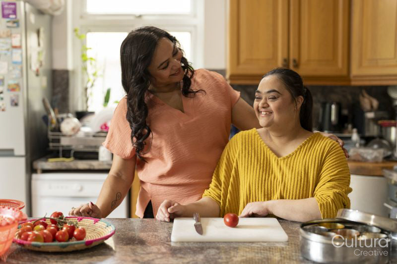 Portrait of mother with down syndrome daughter preparing food in kitchen