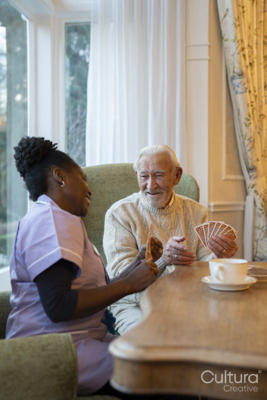 Smiling senior man and nurse playing cards at table in nursing home