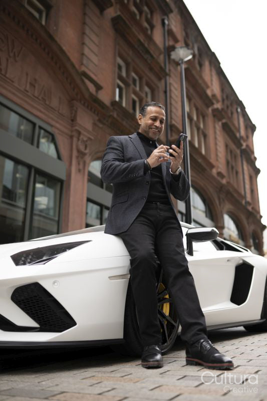 Mature man leaning against luxury car and using phone