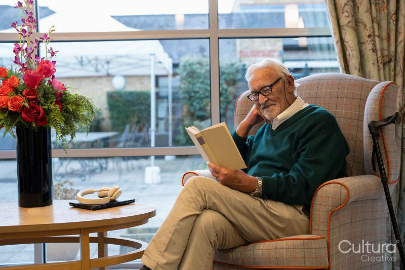 Smiling senior man sitting in armchair and reading book