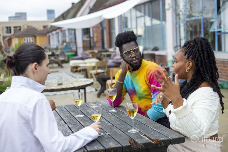 Friends sitting at table, having white wine and talking on rooftop terrace