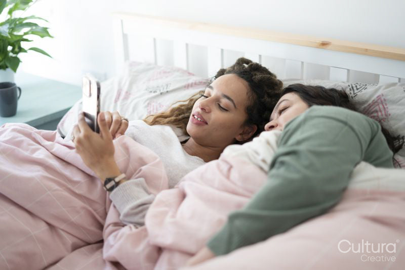 Two women using smartphone in bed