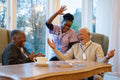 Smiling senior people and nurse playing cards at table in nursing home