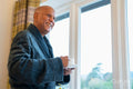 Senior man standing with coffee next to window in his room at nursing home