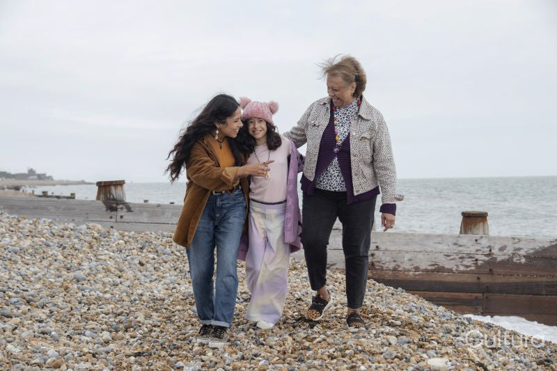 Grandmother, mother and daughter walking on beach on cloudy day