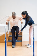 Female therapist assisting senior woman descending steps in exercise room